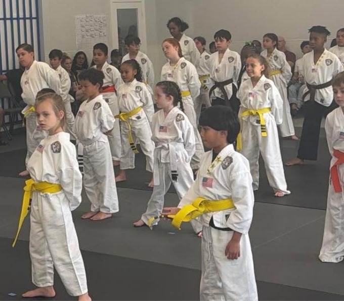 Empower Martial Arts Academy after school students lined up in uniform with yellow, orange and blue belts during a daily Taekwondo class with instructor Mr. Alex in Lake Worth FL