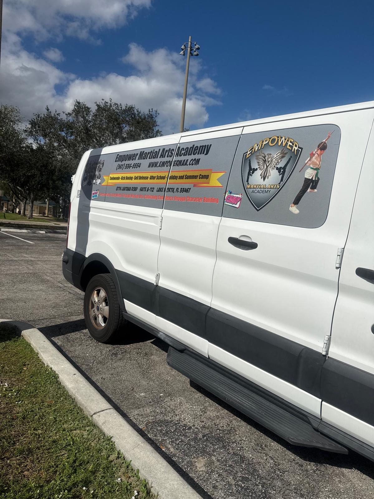 Empower Martial Arts Academy children transportation van #5 — white Ford Transit cargo van with gray side panel featuring academy logo, phone 561-336-5554 and program list, for safe after school pickup in Lake Worth FL